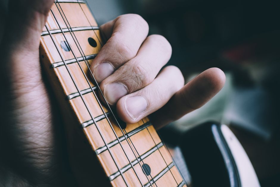 Detailed view of a musician's hand playing chords on an electric guitar fretboard.